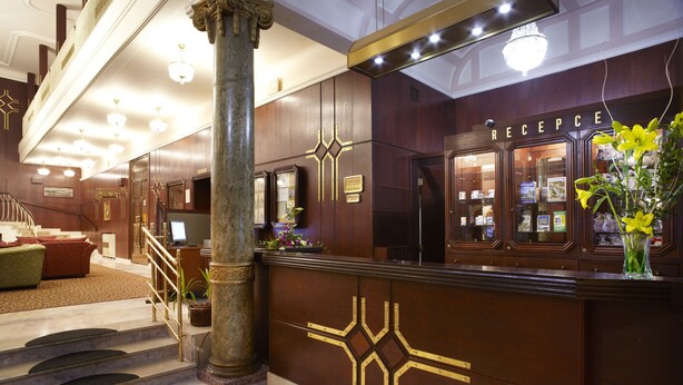 A reception area with a marble staircase, a reception desk, and a chandelier.
