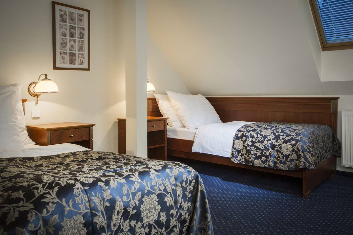 Une chambre d’hôtel avec deux lits, un tableau encadré au mur et une fenêtre avec des stores.