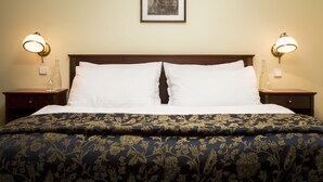 A neatly made bed with a floral-patterned bedspread, two bedside lamps, and a framed picture on the wall.
