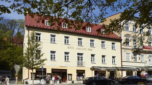 A hotel with a red roof and multiple windows. There are cars parked in front and a person walking on the sidewalk.