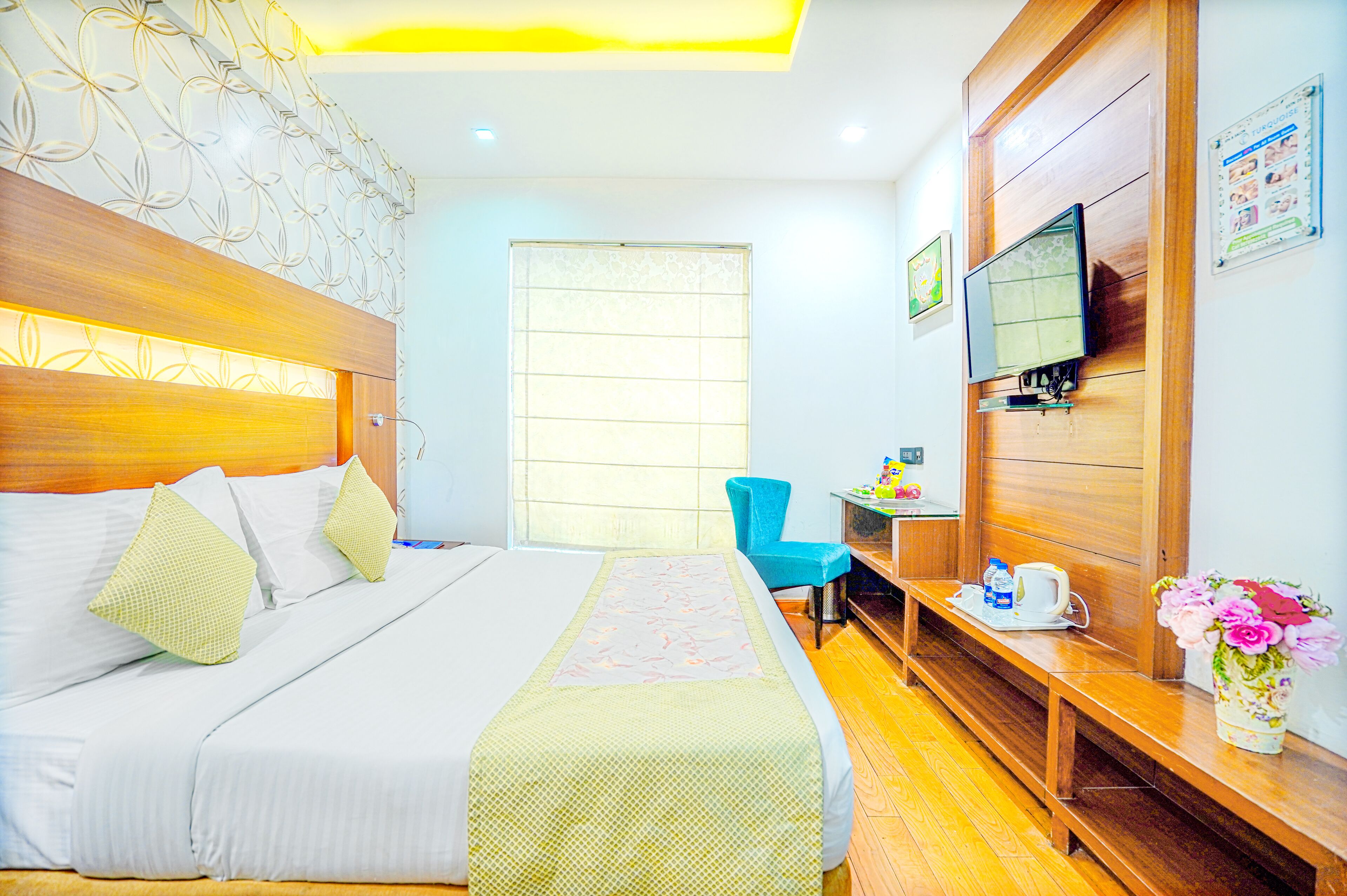 A hotel room with a bed, a desk, a chair, a TV, and a wooden bench.