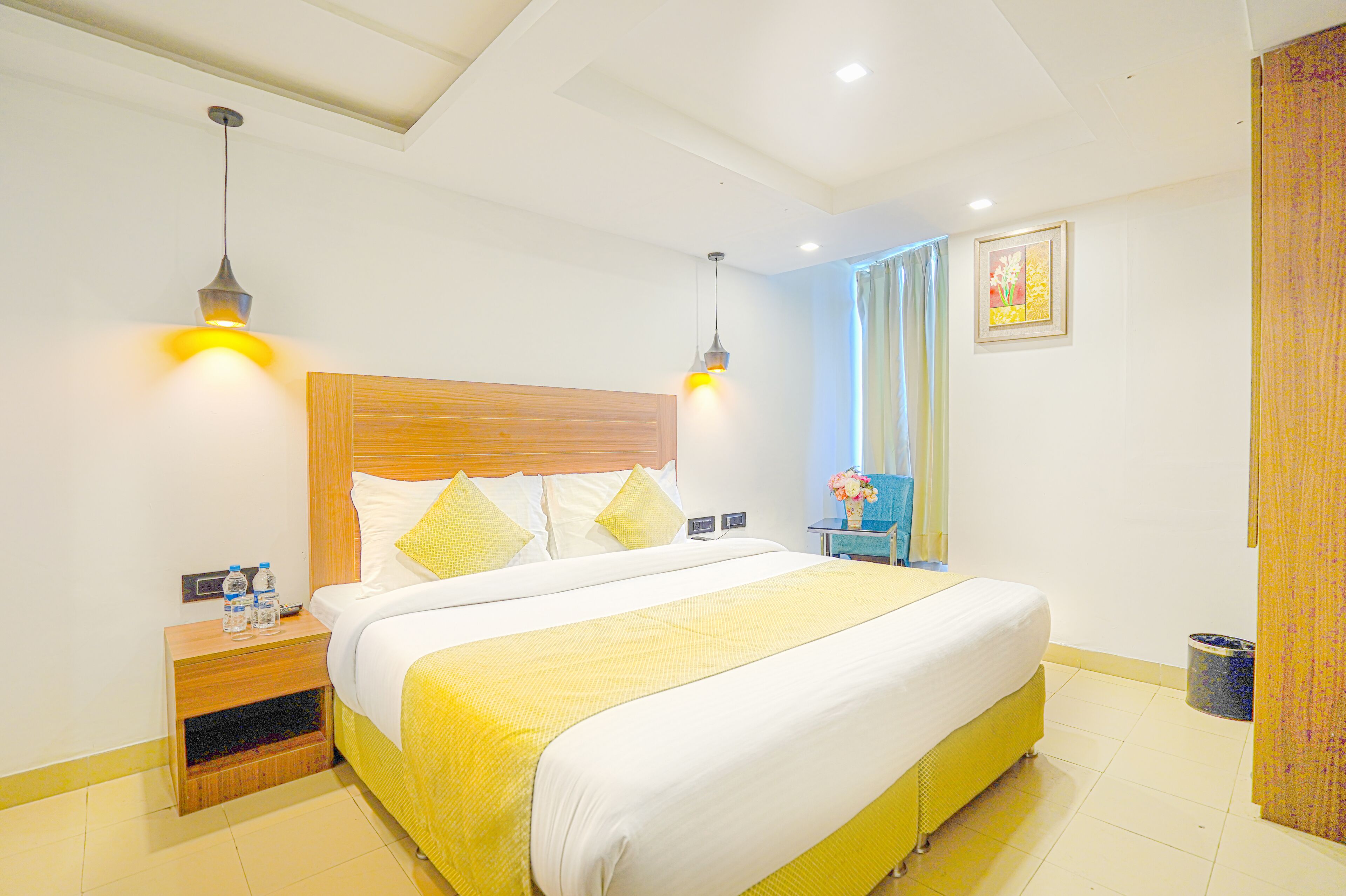 A hotel room with a large bed, two bedside tables, a nightstand, a wooden headboard, and two pendant lights.