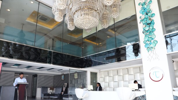 Un hall d’accueil moderne avec un mur de verre, un lustre et un comptoir de réception.