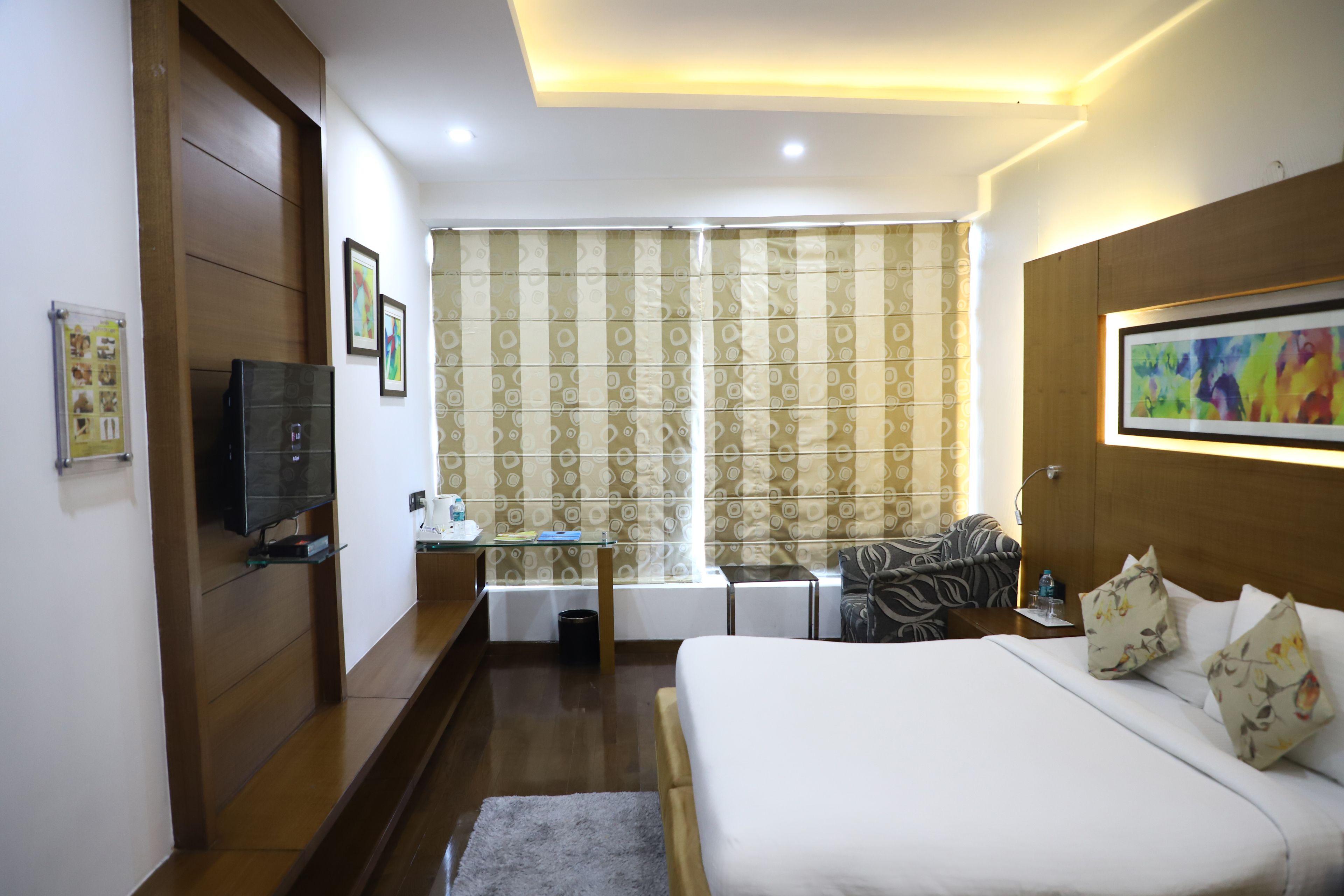 A hotel room with a bed, a desk, a television, and a window with curtains.