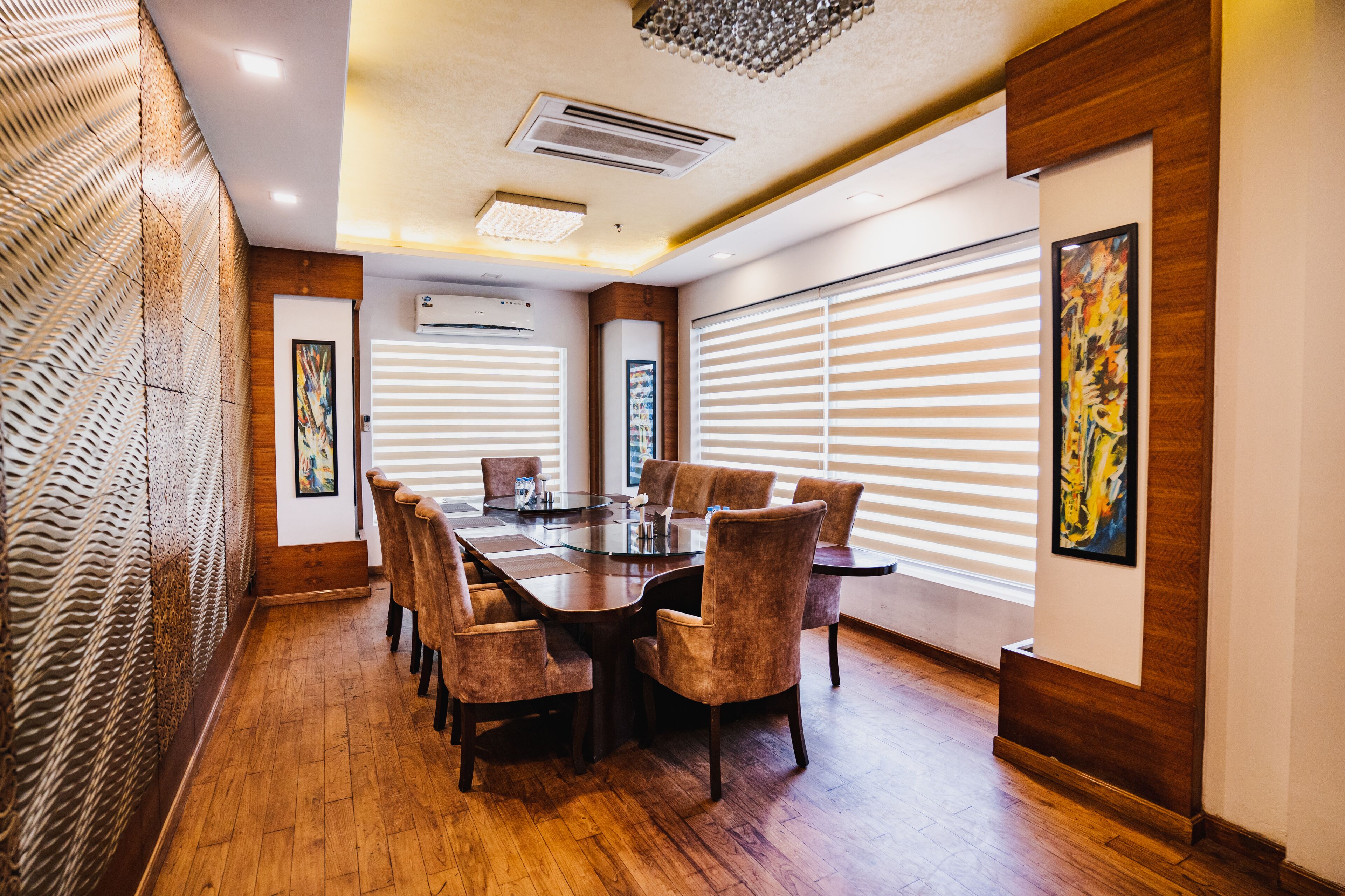A conference room with a large table, chairs, wooden flooring, and a window with blinds.