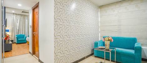 A modern living room with a patterned wall, a teal sofa, and a small table with a vase of flowers.