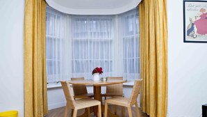 A dining area with a round wooden table, four wicker chairs, and a vase with red flowers.