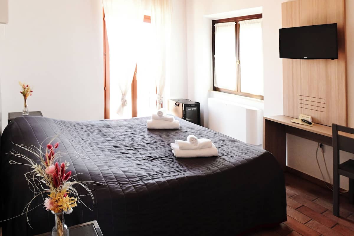 A hotel room with a bed, a desk, a TV, and a window.