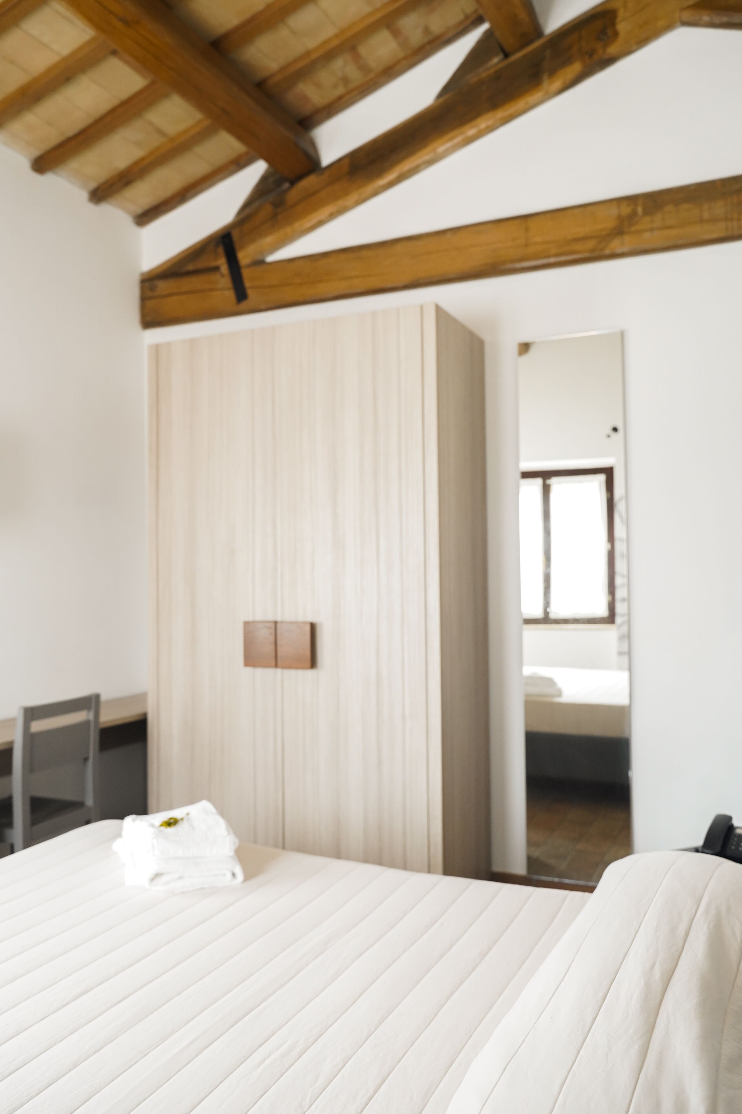 Une chambre à coucher avec un lit, un plafond en bois, une armoire et un miroir qui reflète une fenêtre.