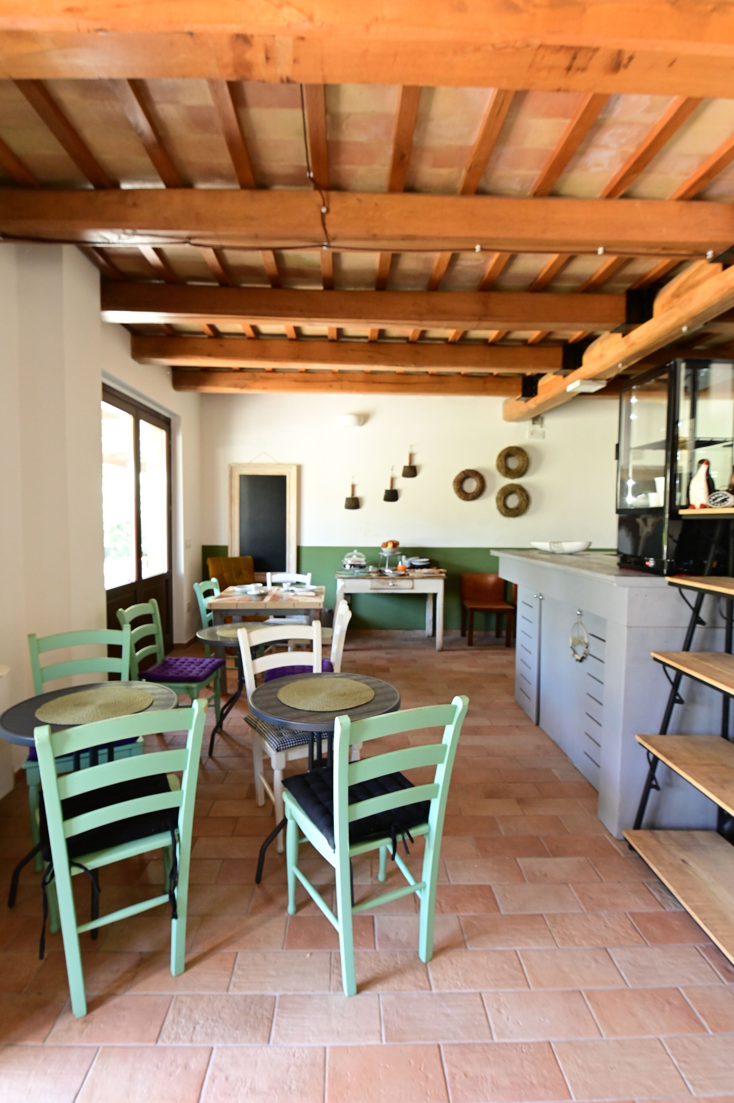 A rustic kitchen with wooden beams, a tiled floor, and a dining area with green chairs and a round table.