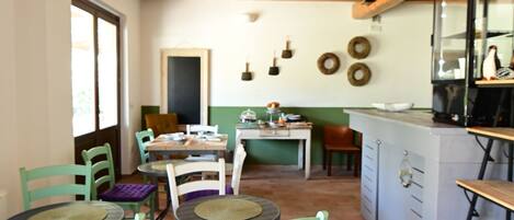 A rustic kitchen with wooden beams, a tiled floor, and a dining area with green chairs and a round table.
