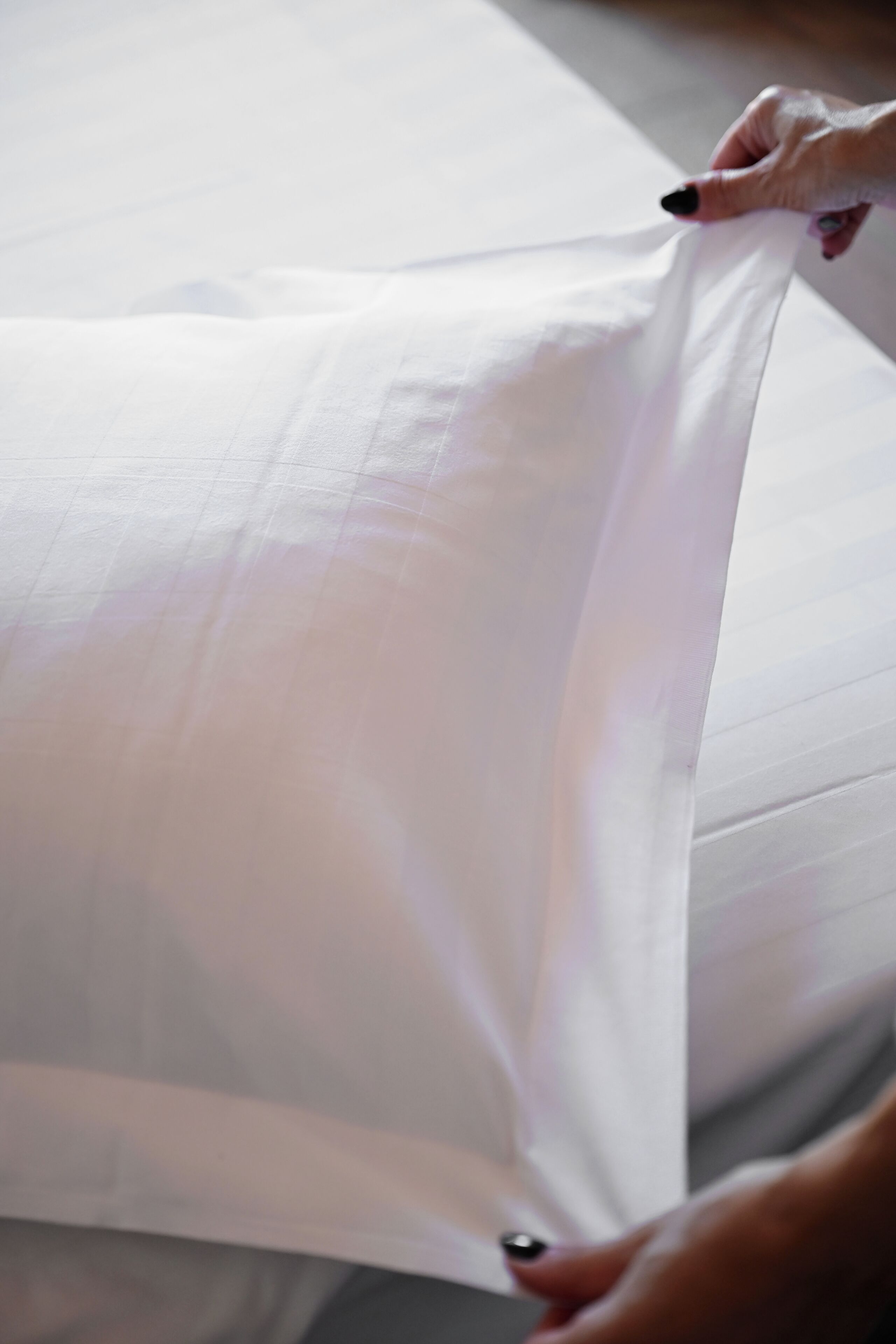 A person adjusting a white pillow on a bed.