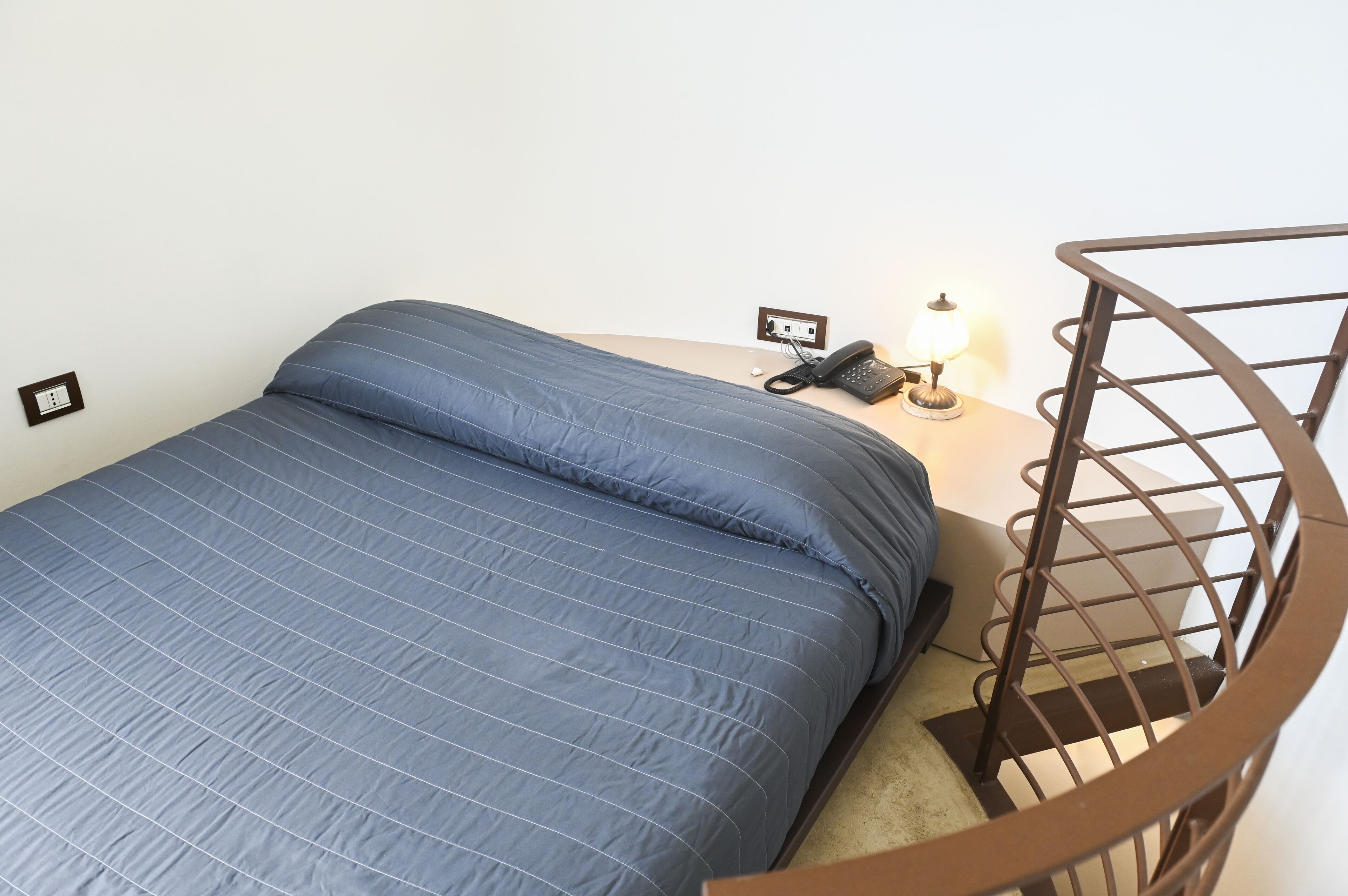 A single bed with a blue quilt, a bedside table with a lamp, and a phone.