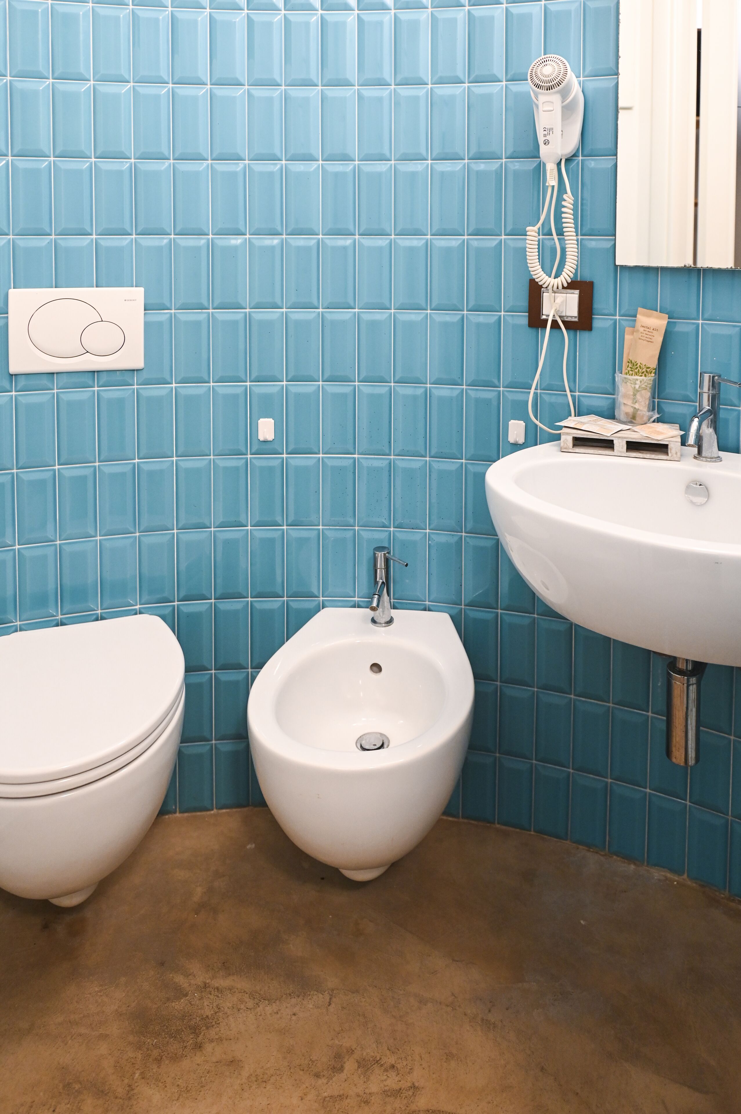 A bathroom with blue tiles, a white toilet, a bidet, and a sink with a mirror.