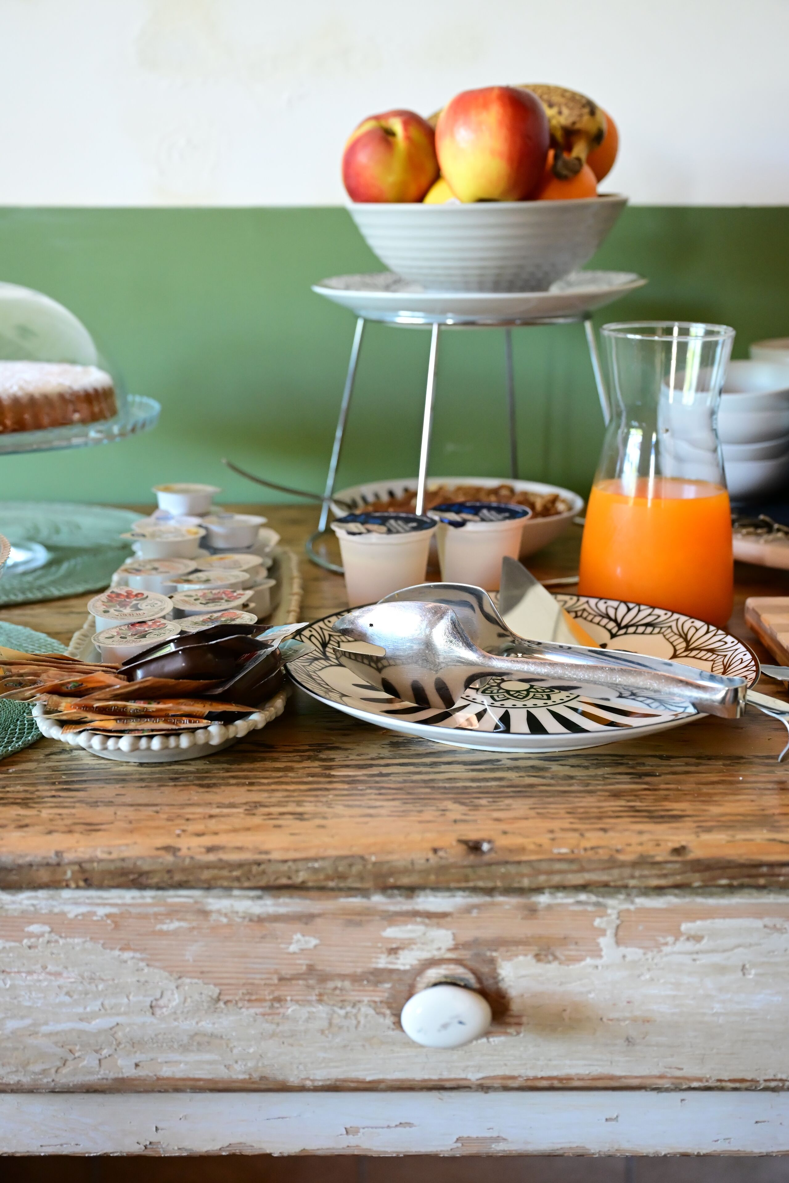 A breakfast setting with a fruit bowl, cereal bowls, a glass of orange juice, and a variety of breakfast items on a wooden table.