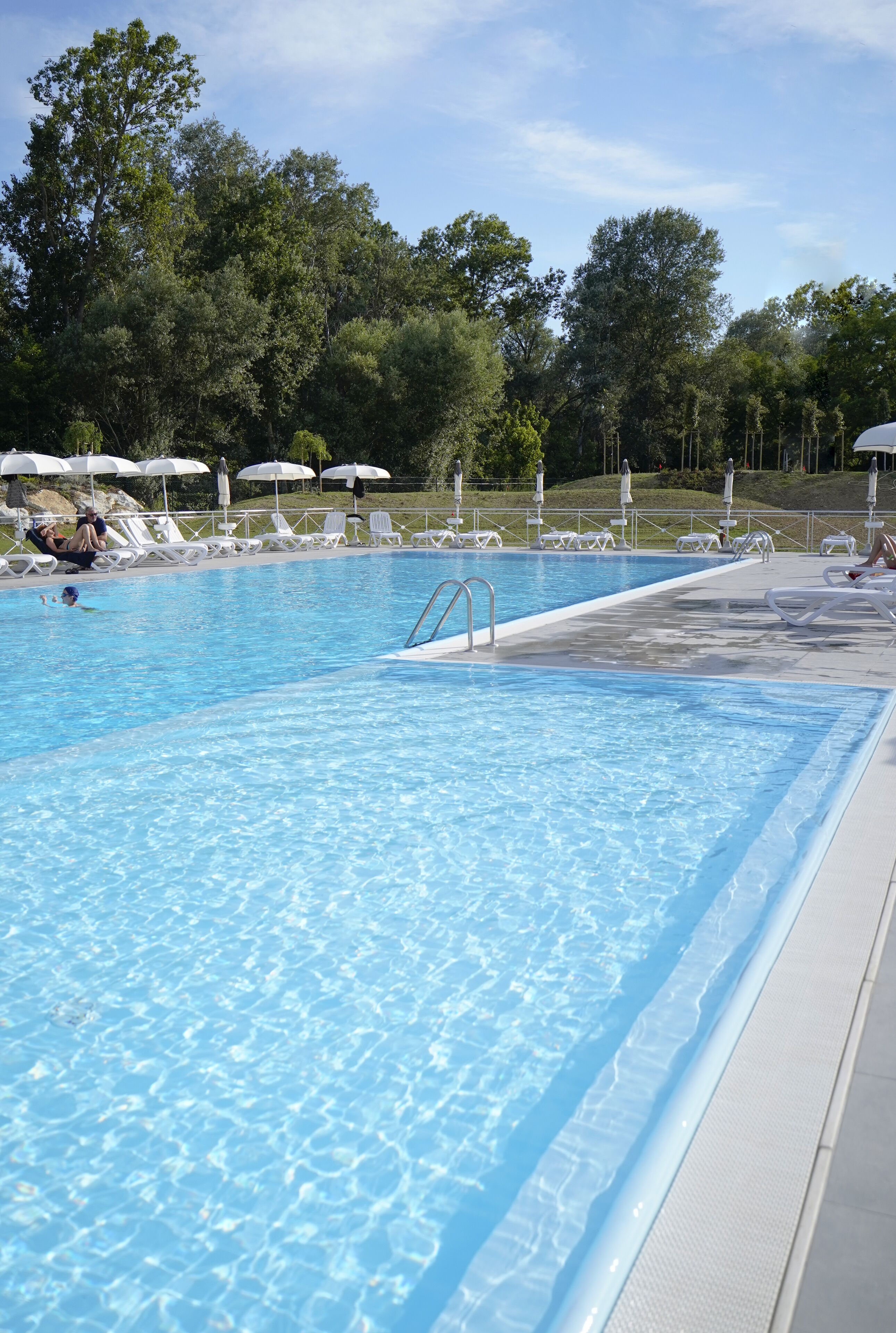 A clear swimming pool with lounge chairs and umbrellas around it.