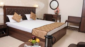 Quarto de hotel com uma cama grande, mesa de cabeceira com abajur, escrivaninha e uma cadeira.