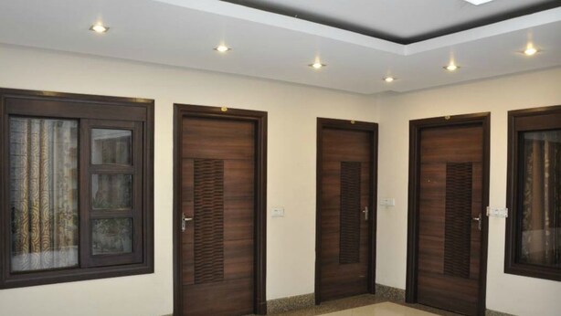 Um corredor com quatro portas de madeira, cada uma com um janelão acima. O chão é ladrilhado e o teto possui iluminação embutida.