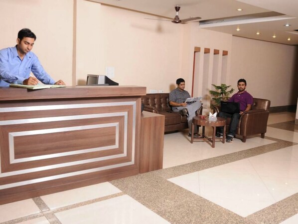 A reception area with a wooden reception desk, a seating area with sofas and a small table, and a ceiling fan.
