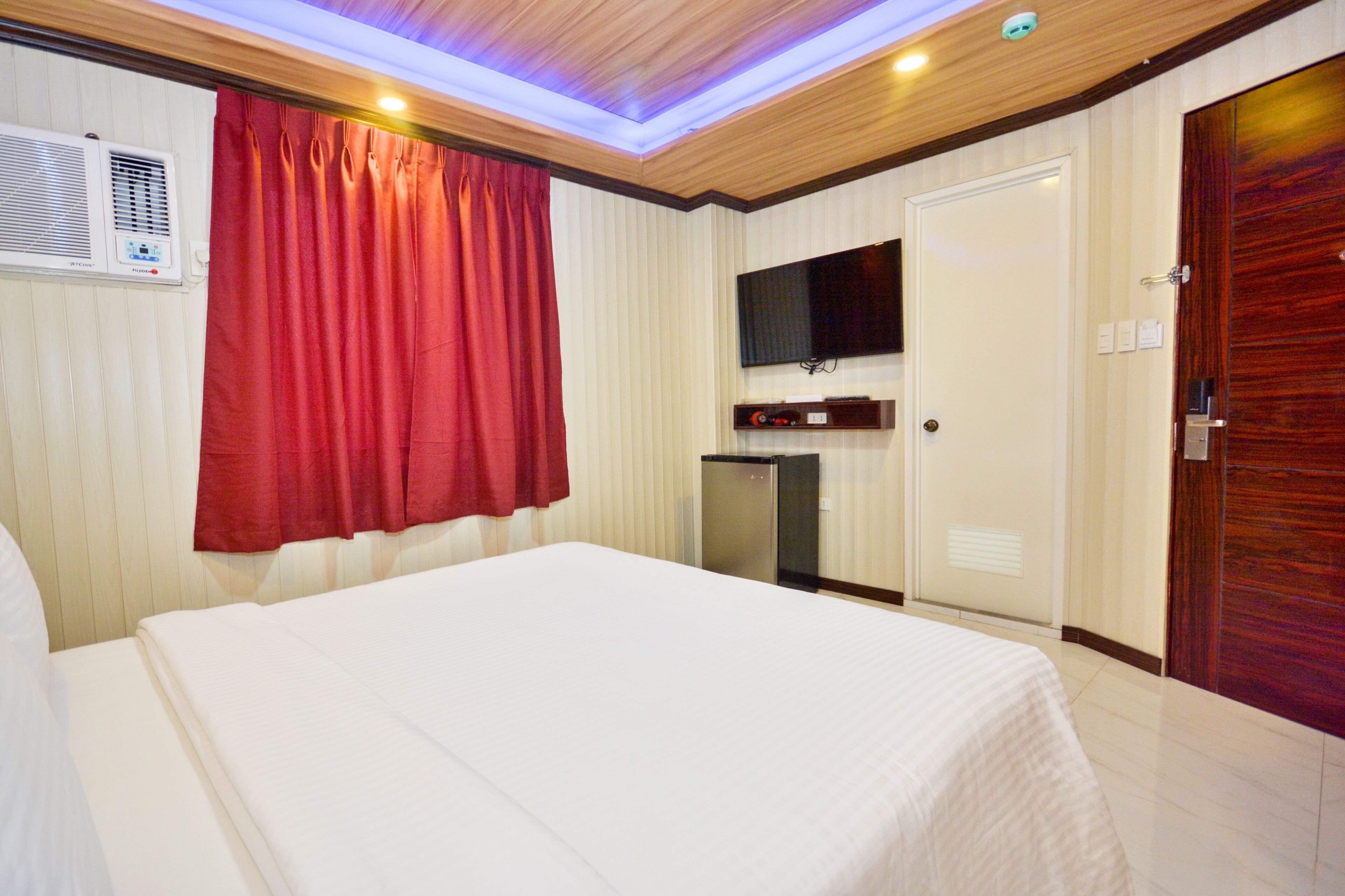 A hotel room with a bed, a television mounted on the wall, a small desk, and a door.