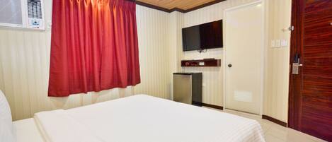 A hotel room with a bed, a television mounted on the wall, a small desk, and a door.