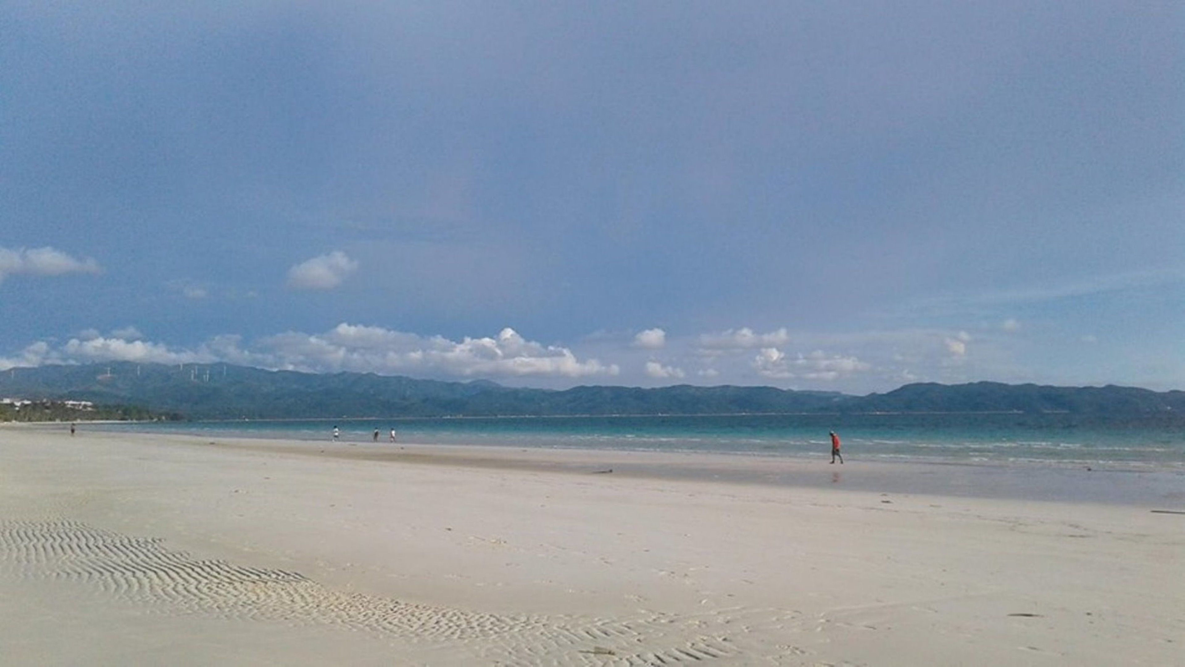 A wide sandy beach with a clear sky and distant mountains.