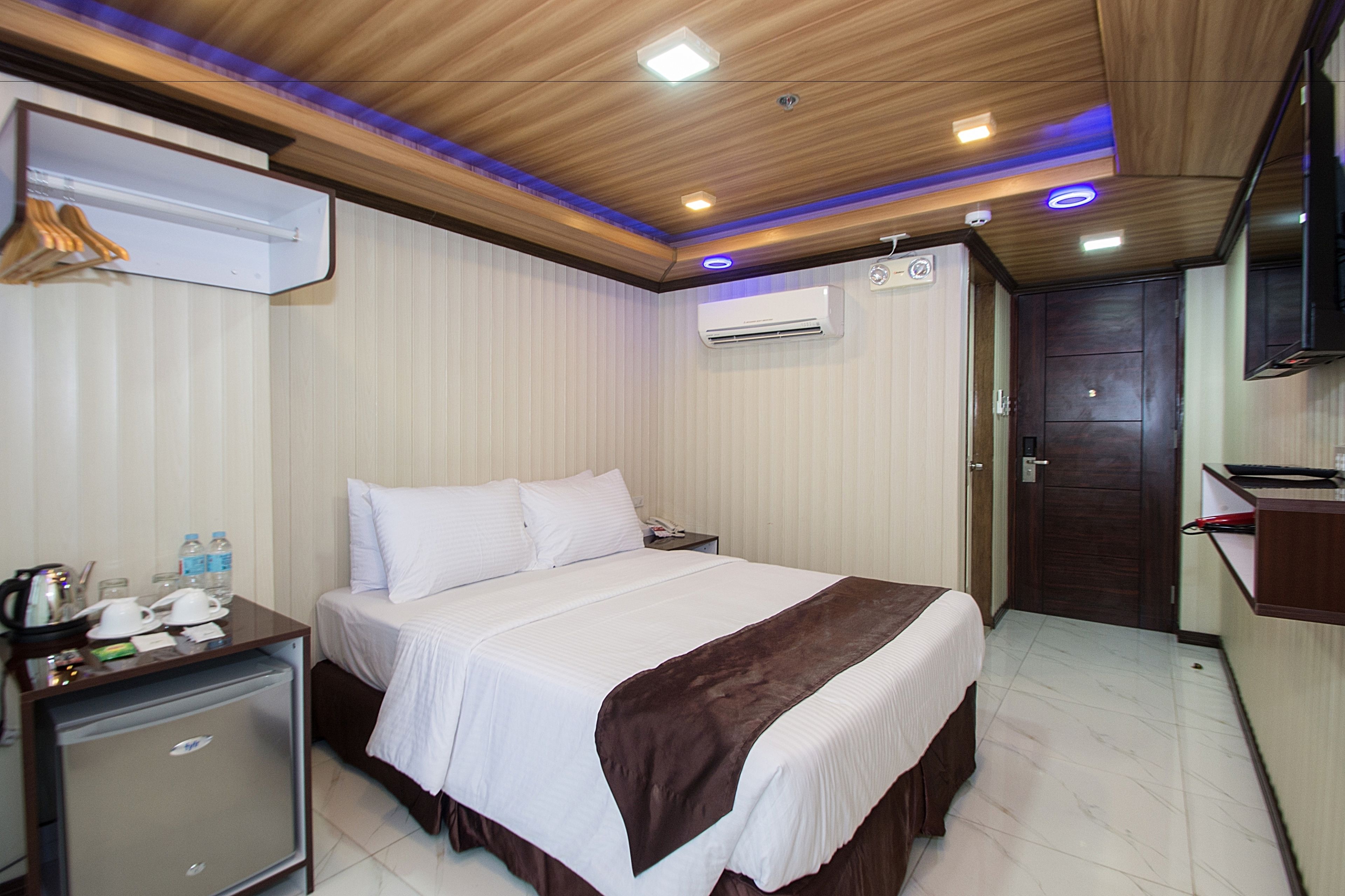Una habitación de hotel con cama, mesita de noche y pequeño escritorio con refrigerador.