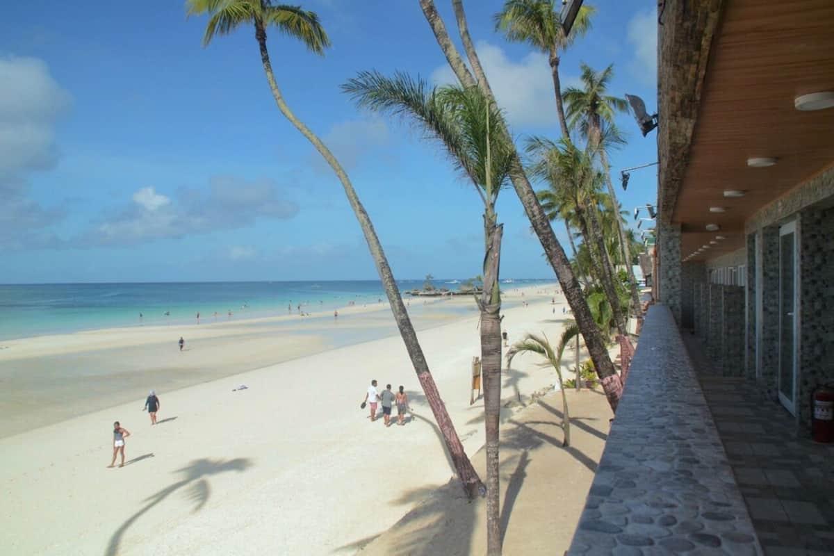 A beach with palm trees, a clear sky, and a building with a stone facade.