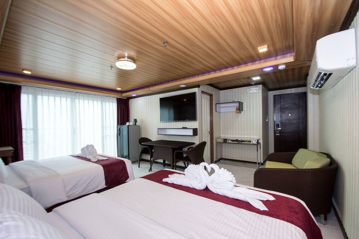 A hotel room with two beds, a desk, a chair, and a television.