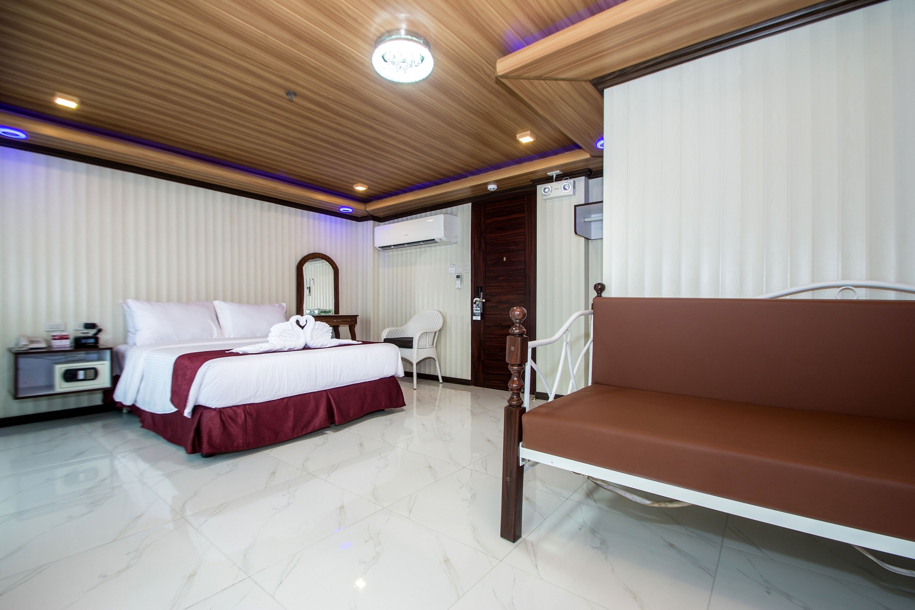 Habitación de hotel con una cama, un sofá, una mesita de noche, una silla y un equipo de aire acondicionado.