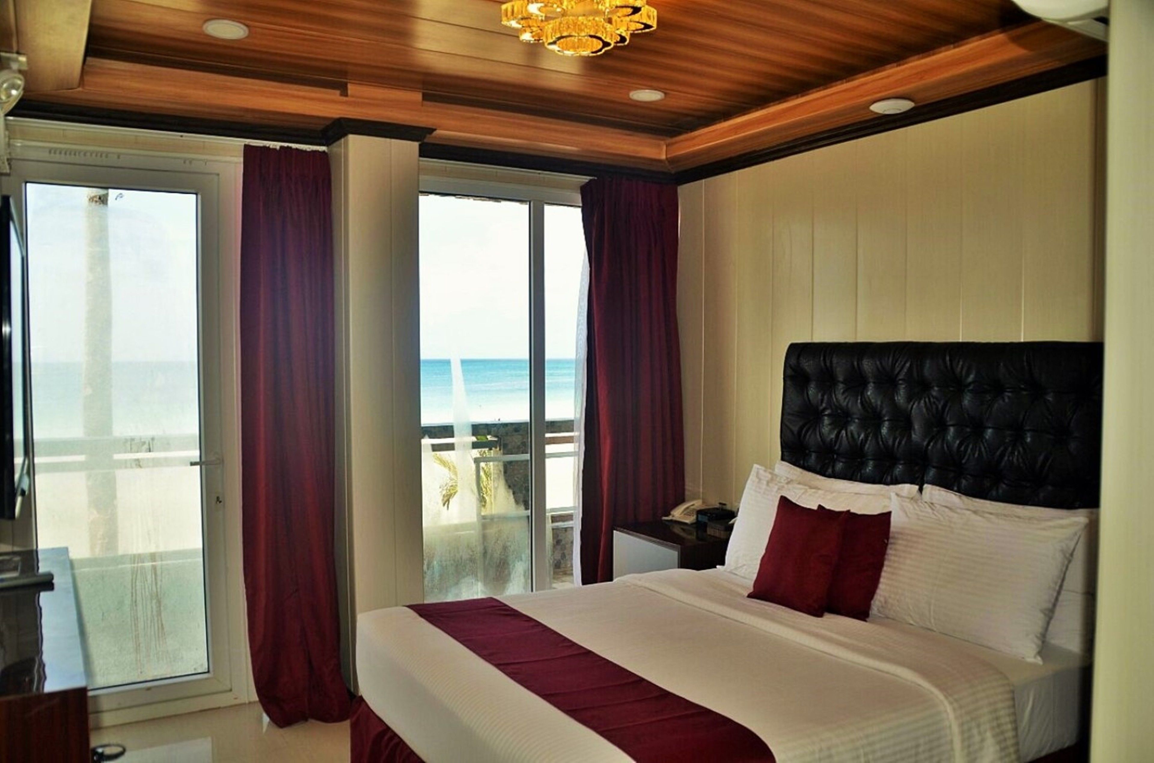 A hotel room with a large bed, a view of the sea through a sliding door, and a wooden ceiling.