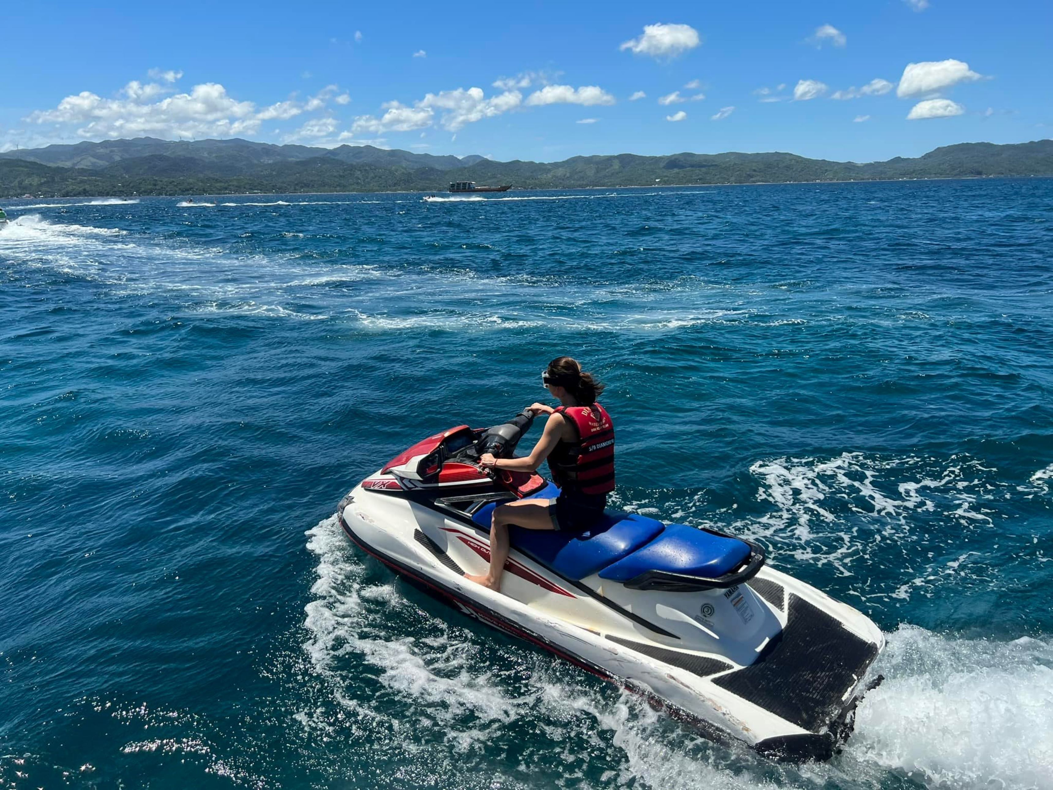 En person kører jetski på vandet med bjerge i baggrunden.
