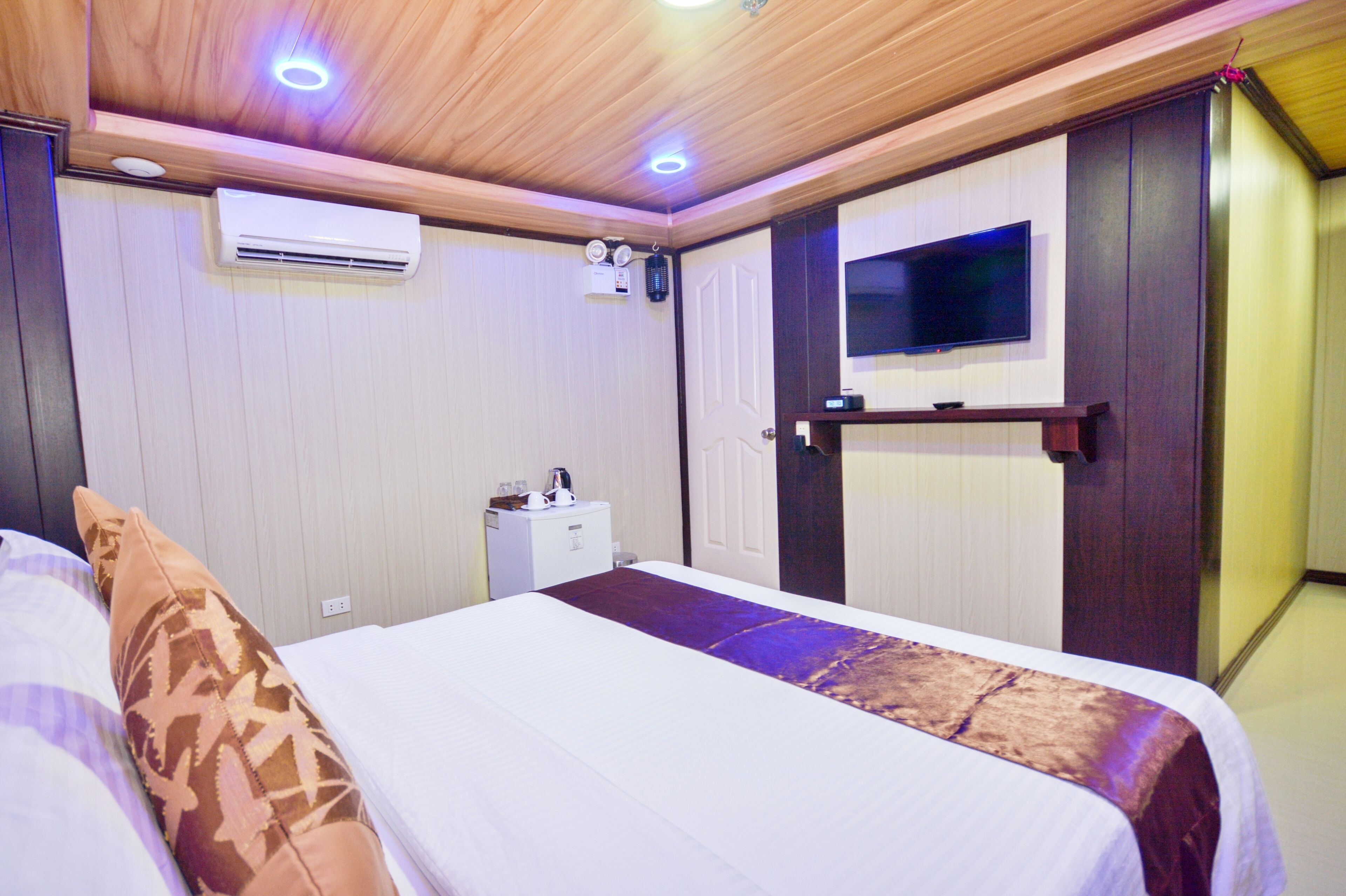 Habitación de hotel con cama, televisor montado en la pared, aire acondicionado y una mesita de noche.