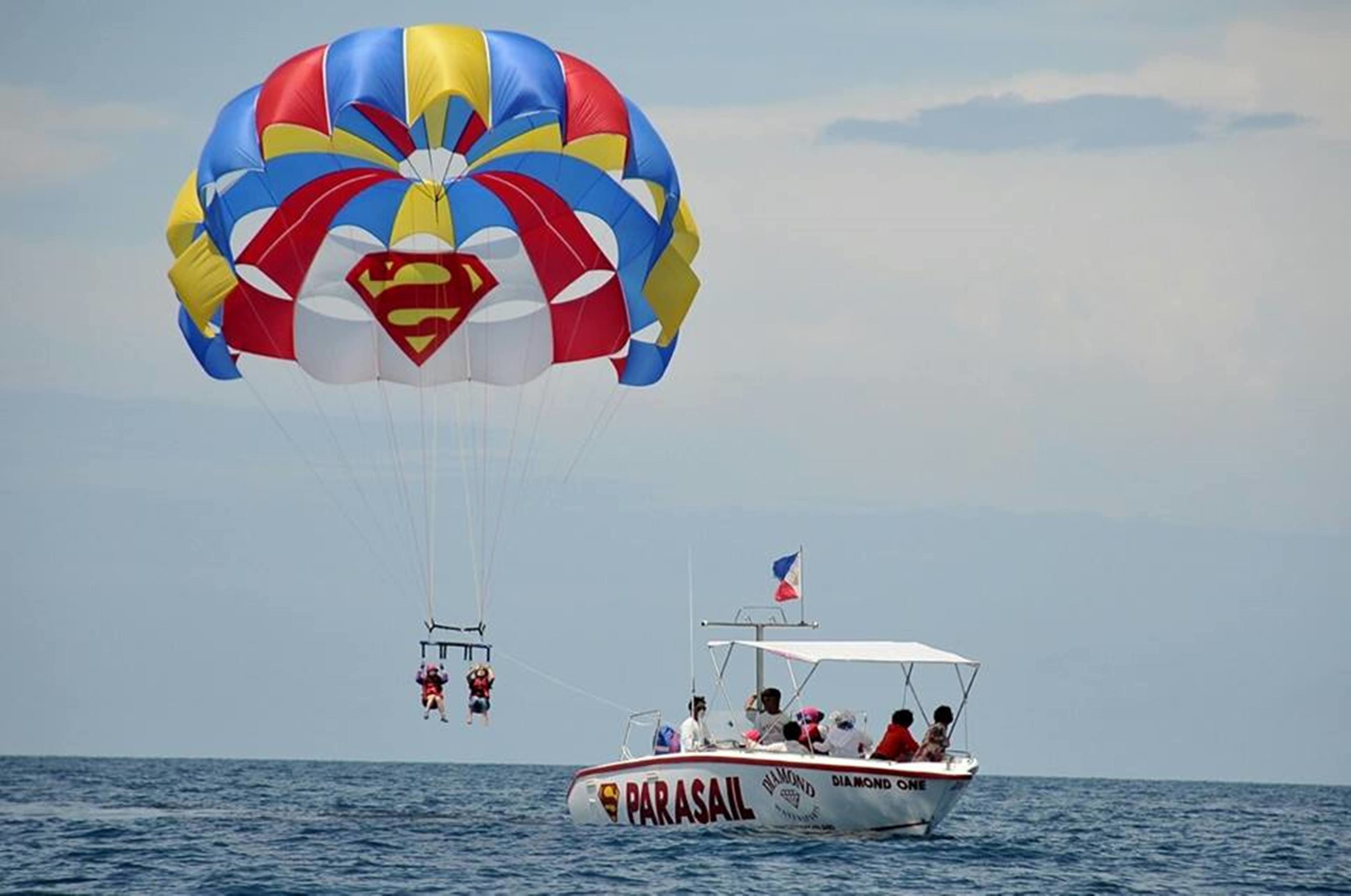 A parasail with a Superman logo, a boat with 'PARASAIL' and 'DIAMOND ONE' written on it, and a flag on the boat.