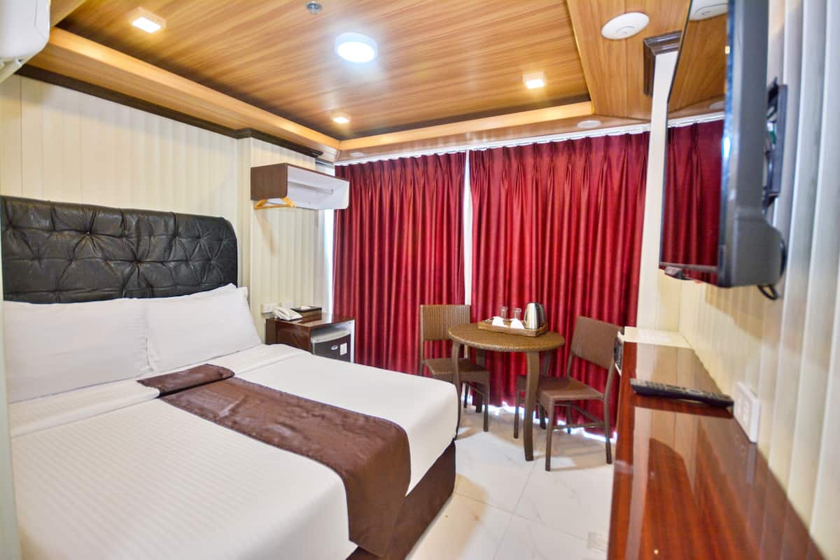 A hotel room with a large bed, a desk with a chair, a small table, and a TV mounted on the wall.