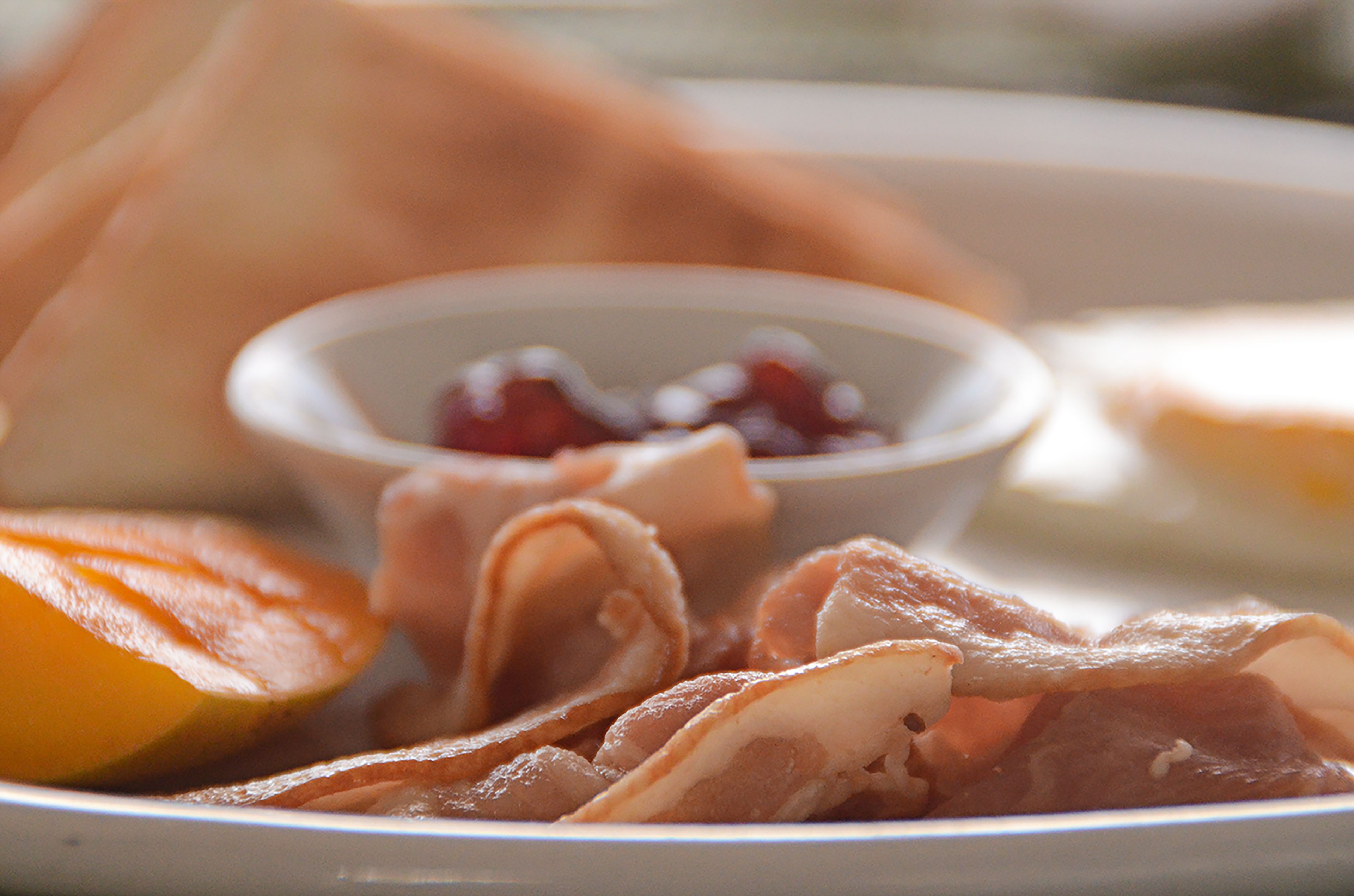 Une assiette avec des tranches de viande, un fruit et un petit bol de confiture.