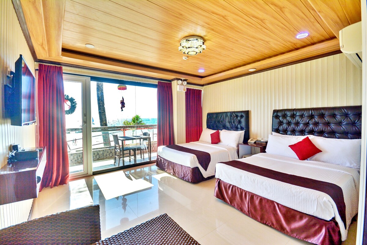 Habitación de hotel con dos camas, puerta de vidrio que da a un balcón, techo de madera y un candelabro.