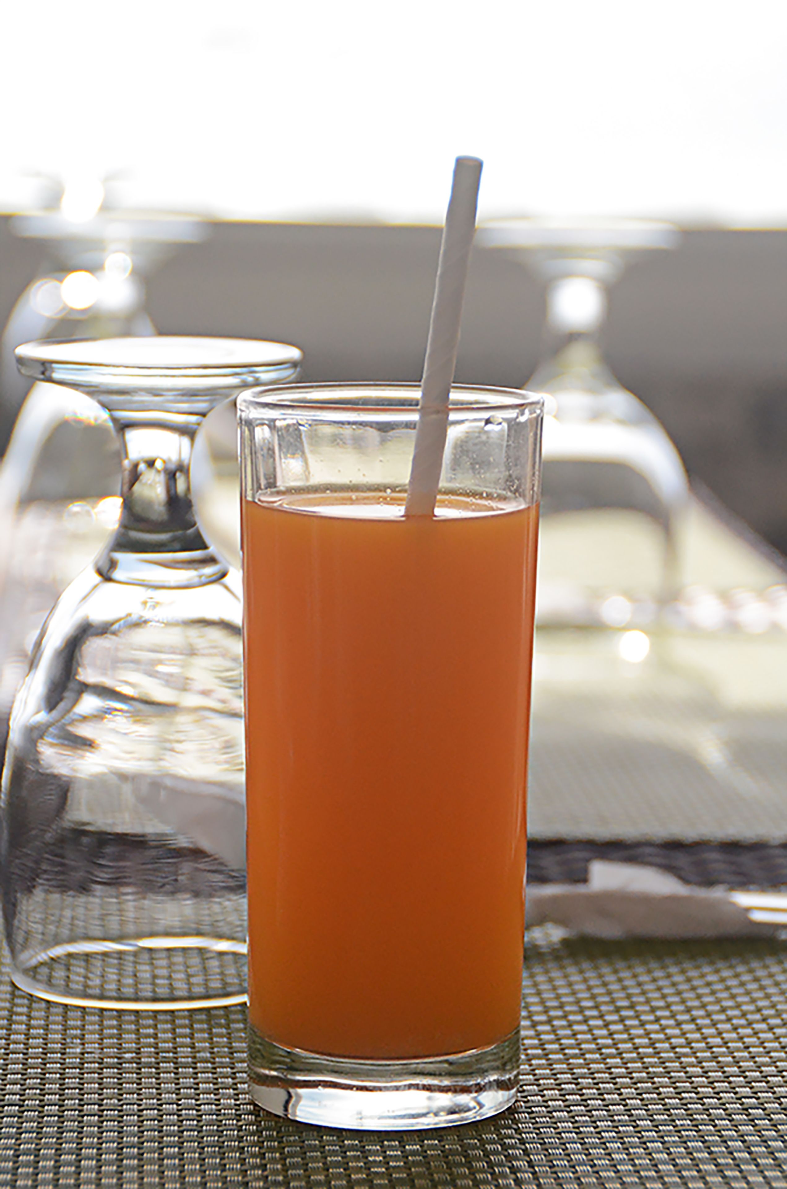 A glass of orange juice with a straw on a table.