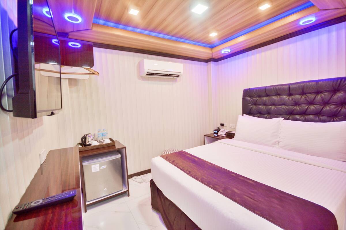 A hotel room with a bed, bedside table, and a small refrigerator.