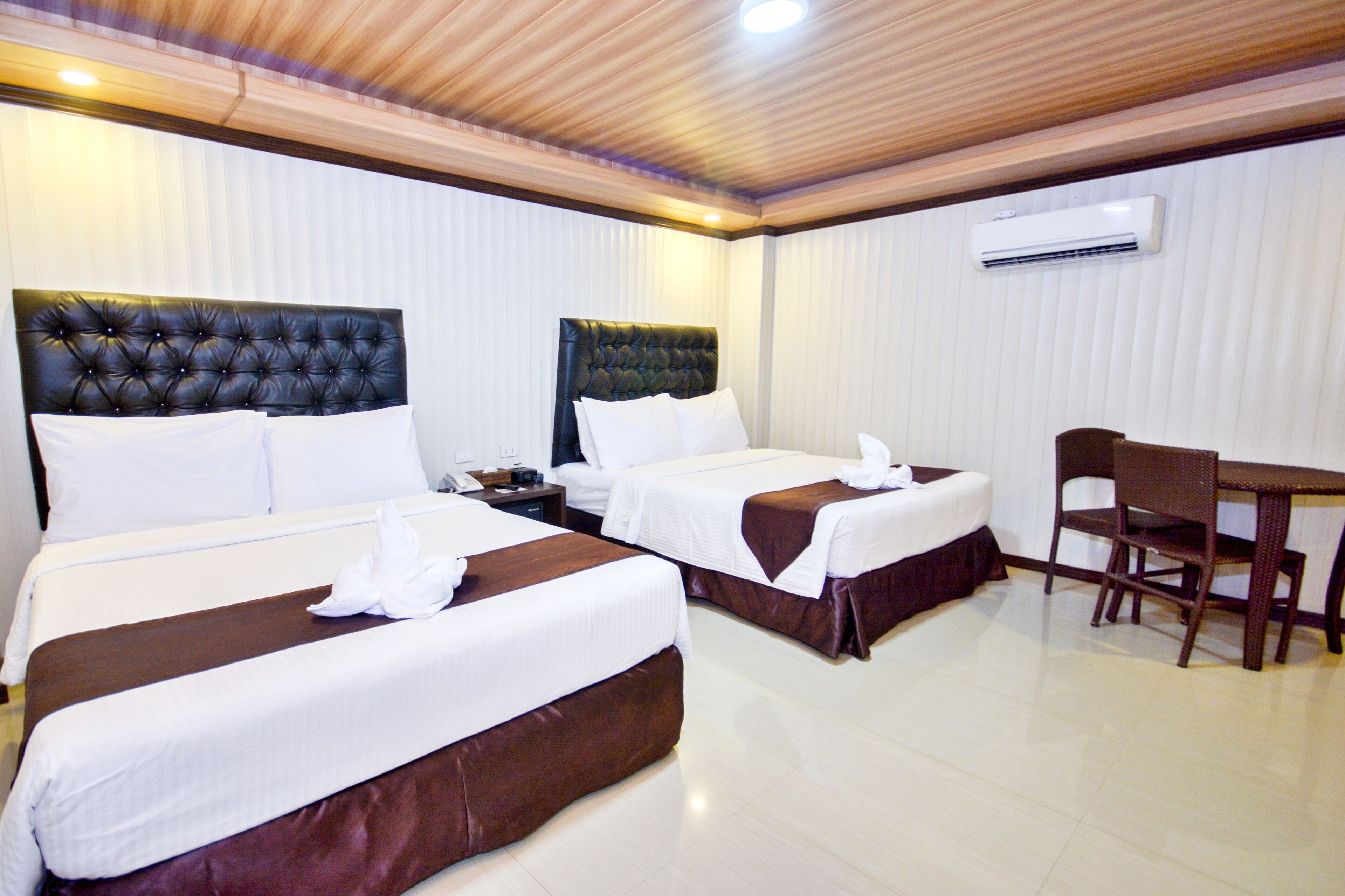 A hotel room with two beds, a desk, and an air conditioning unit.