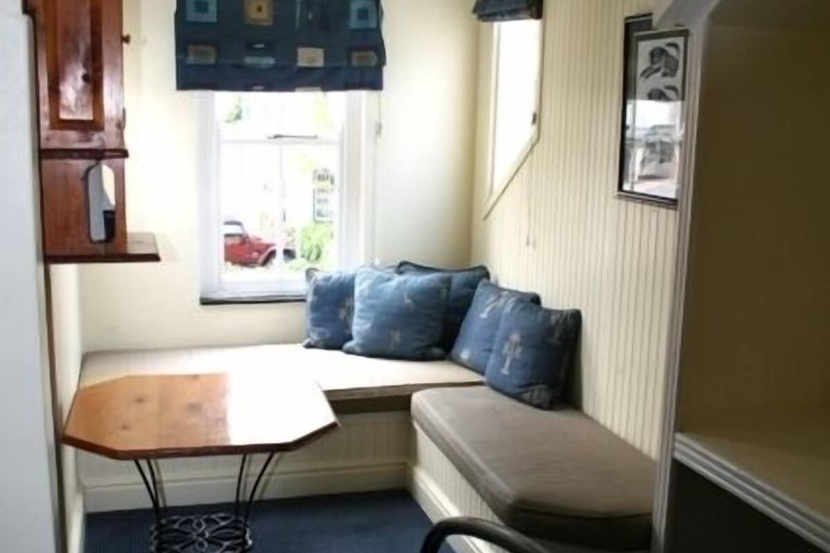 A compact room with a bed, a small table, a bench, and a window with a view of the outside.