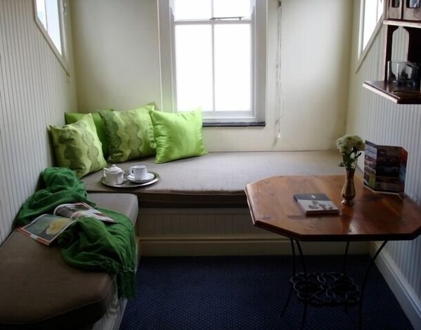 A cozy reading nook with a cushioned bench, a small table with a book, and a window with a view.