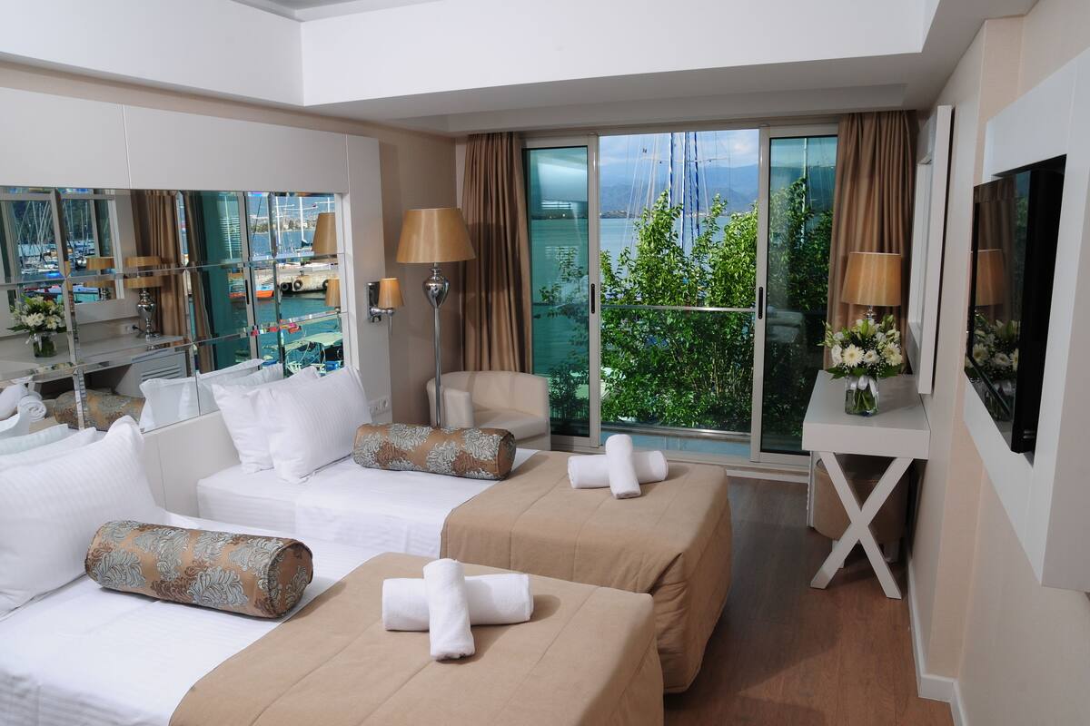 A hotel room with a bed, two sofas, a TV, a desk, and a balcony with a view of the sea.