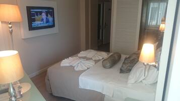 A hotel room with a bed, two lamps, a TV on the wall, and a door in the background.