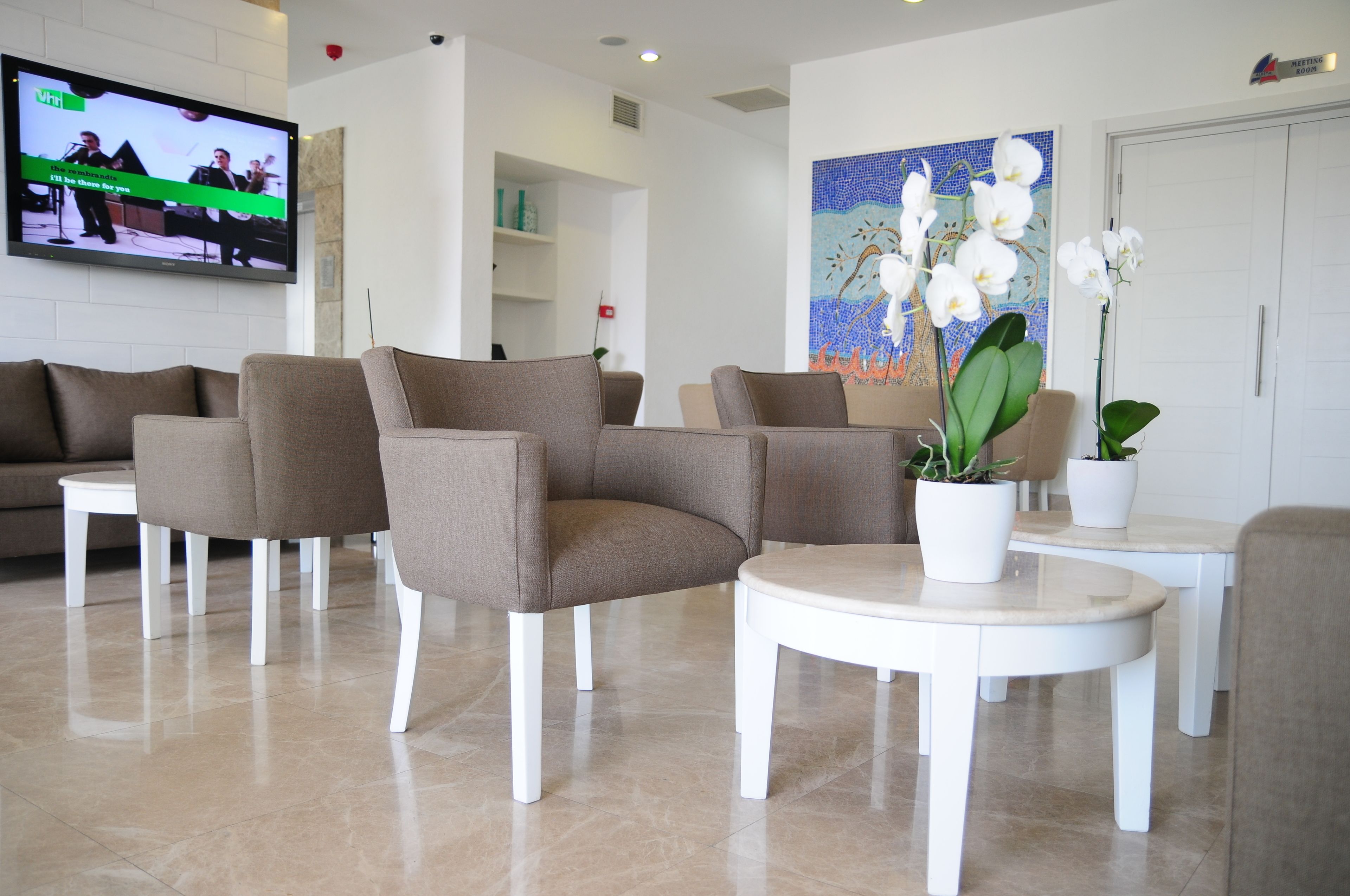 Eine moderne Lobby mit Sitzgelegenheiten, einem Fernseher, der eine Bandvorführung zeigt, und einem dekorativen Gemälde.