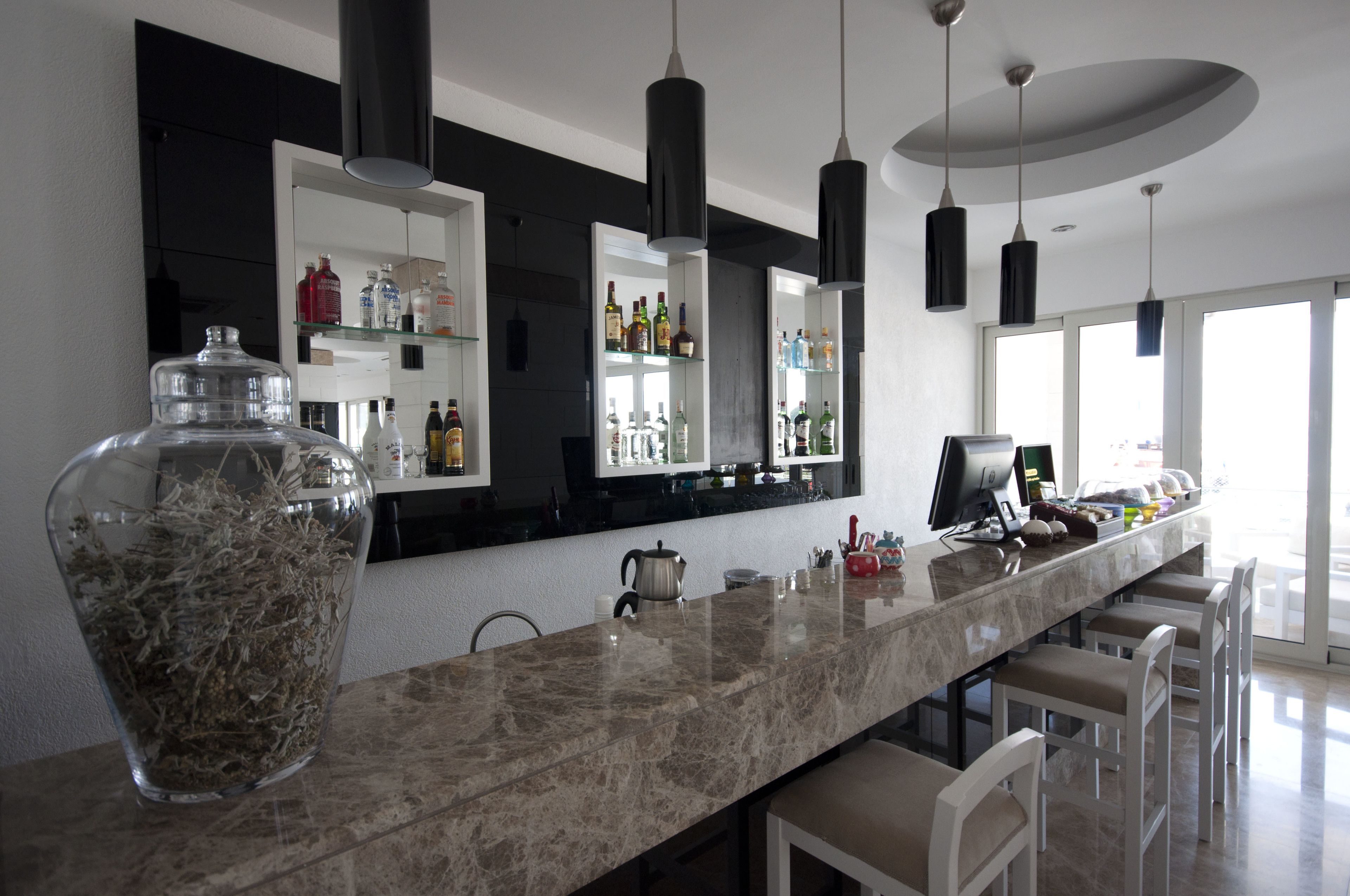 A modern kitchen with a marble countertop, black pendant lights, and a large window.