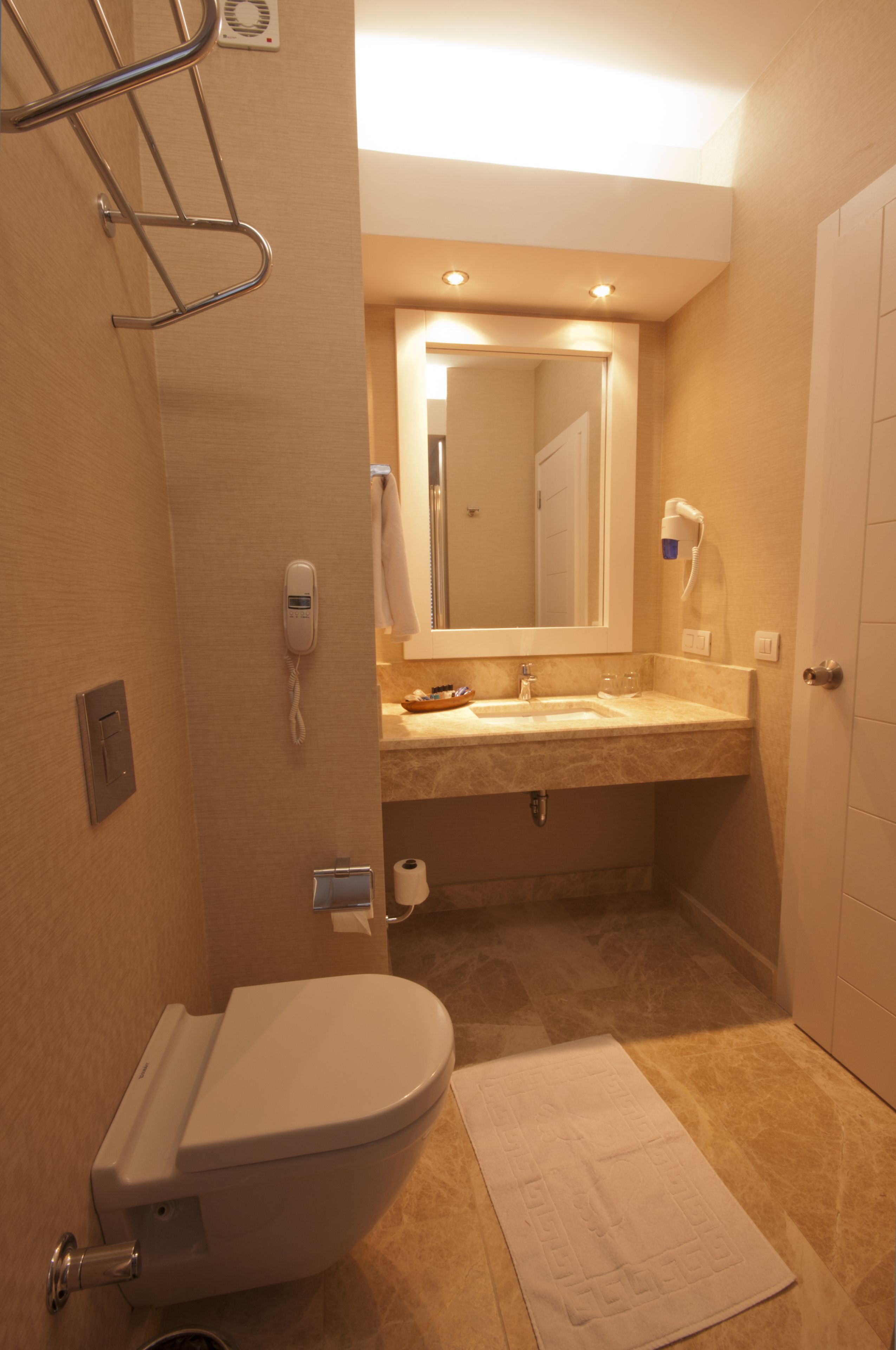 Un baño con inodoro, lavamanos, espejo y toallero.