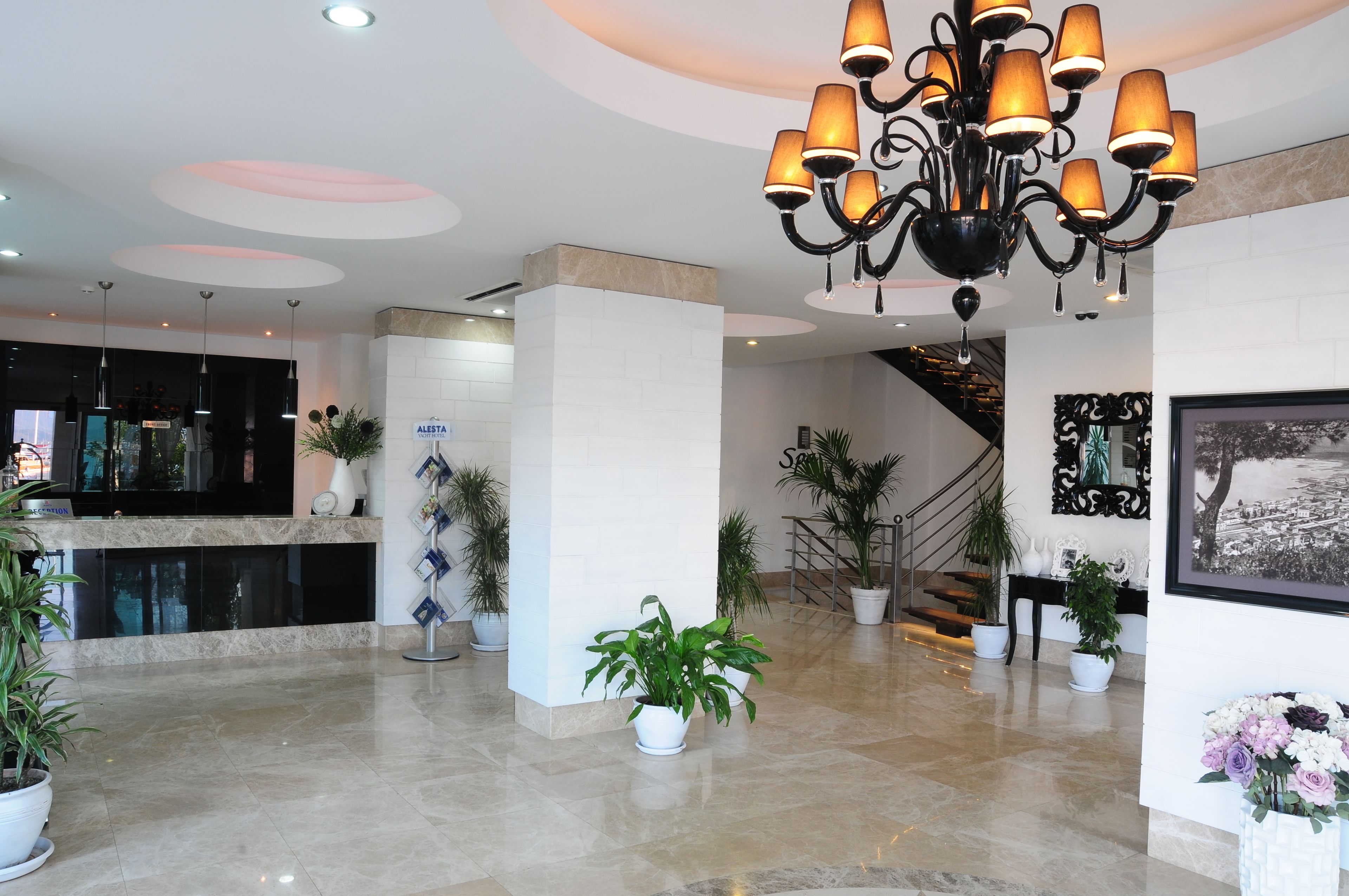 A modern lobby with a chandelier, potted plants, a reception desk, and a staircase.