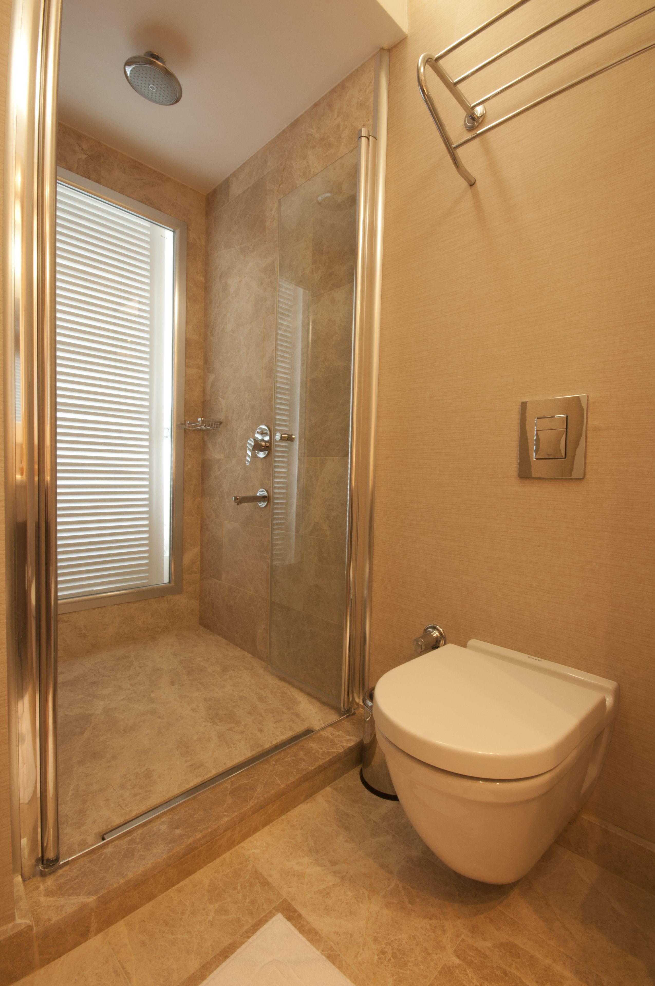 A bathroom with a shower, toilet, and a window with blinds.