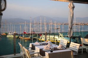Ein Essbereich mit gedeckten Tischen, mit Blick auf eine Marina und Segelboote.